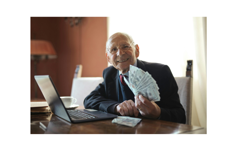 Hombre de negocios anciano demostrando el crecimiento del comercio electrónico, sonriendo con efectivo en la mano en su computadora portátil.